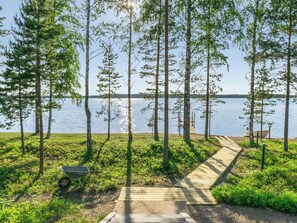 A wooden pathway leading to a dock by a calm lake, surrounded by tall trees and greenery.