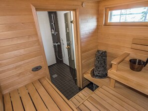 A sauna room with wooden walls, a glass door leading to a shower area, and a window.