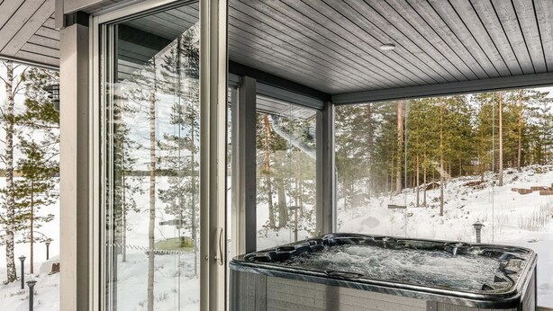 A glass-enclosed hot tub area with a view of a snowy landscape and trees.