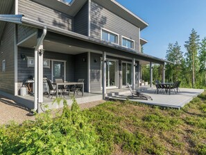 Et moderne hus med to etager og en overdækket terrasse med udendørs møbler.