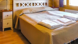 A neatly made bed with a quilted bedspread, two bedside lamps, a nightstand with a drawer, and a window with curtains.