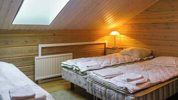 A small, cozy room with a sloped ceiling and a skylight, featuring a bed with a quilted blanket and pillows, a bedside table with a lamp, and a radiator.