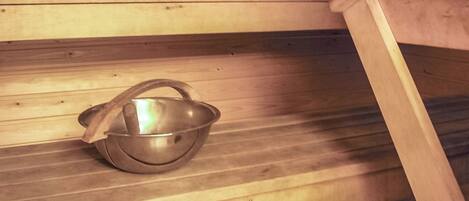 Een sauna met een metalen wasbak op een houten bank.