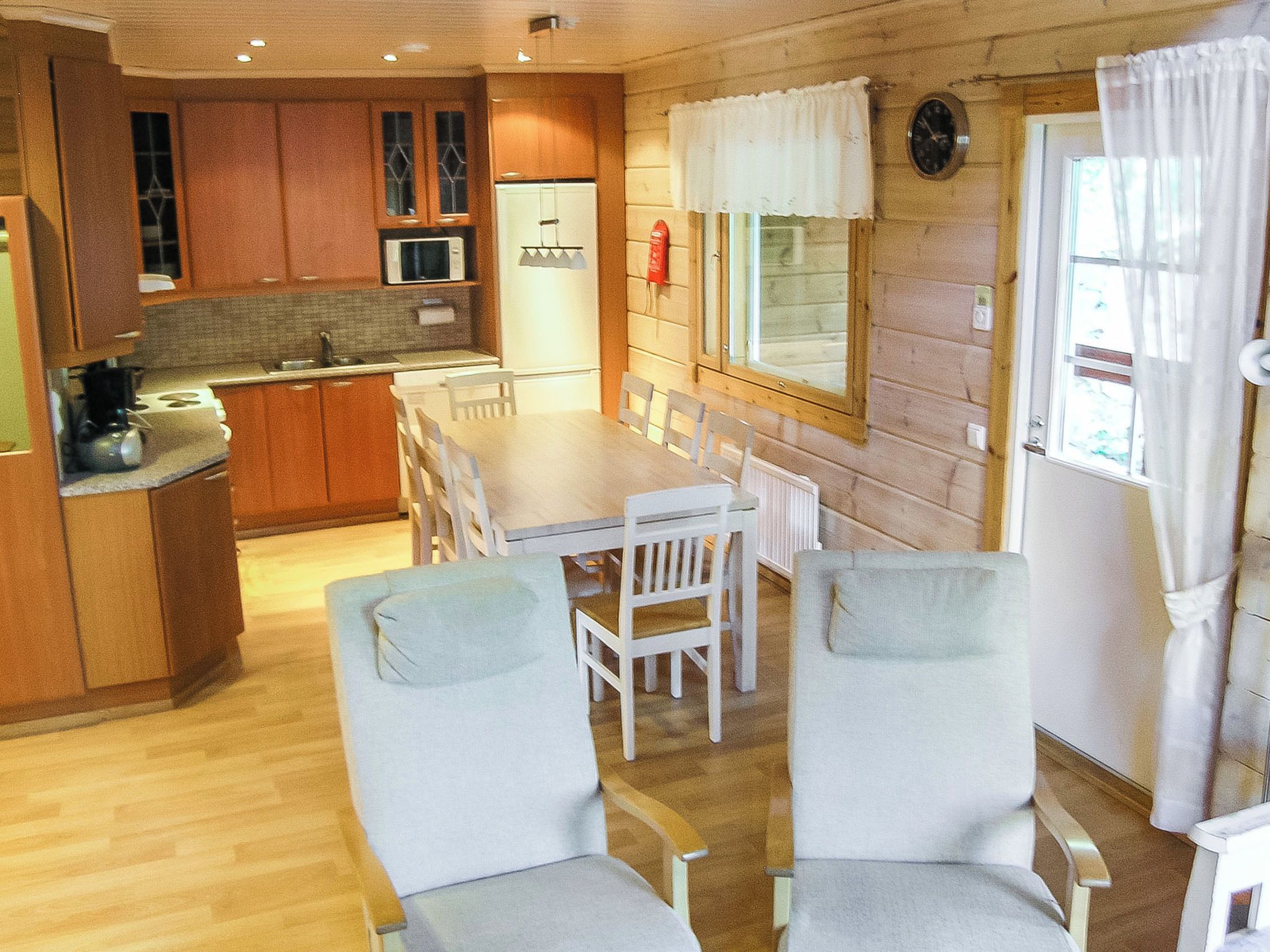 Cocina compacta con armarios de madera, microondas y comedor con mesa y sillas.