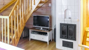 A room with a wooden staircase, a television on a white stand, and a fireplace.