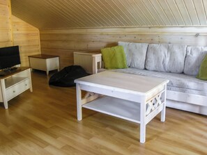 A room with a white sofa, a television on a stand, a small table, and a radiator.