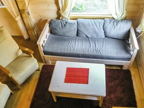 Een kamer met een grijze bank, een witte tafel met een rode placemat, een houten stoel en een raam met gordijnen.