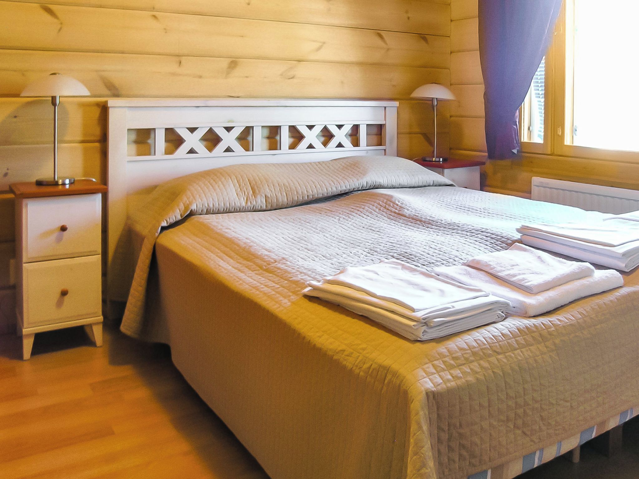 A neatly made bed with a white headboard, two bedside lamps, and a wooden nightstand with a drawer.