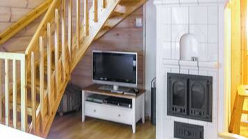 Una habitación con escalera de madera, televisor sobre un mueble y chimenea.