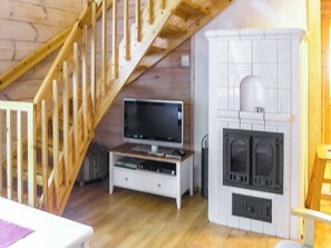 A room with a wooden staircase, a television on a stand, and a fireplace.