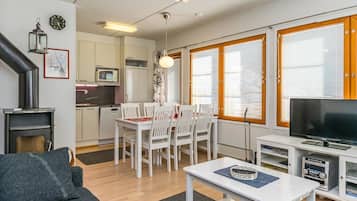 A modern living room with a sofa, a dining table with chairs, a TV, and a kitchen area with cabinets and a microwave.