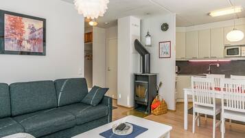 A modern living room with a sofa, a coffee table, a fireplace, and a kitchen area with white cabinets and a microwave.