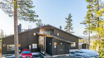 A modern two-story building with a garage, a red car parked in front, and a snowy landscape.
