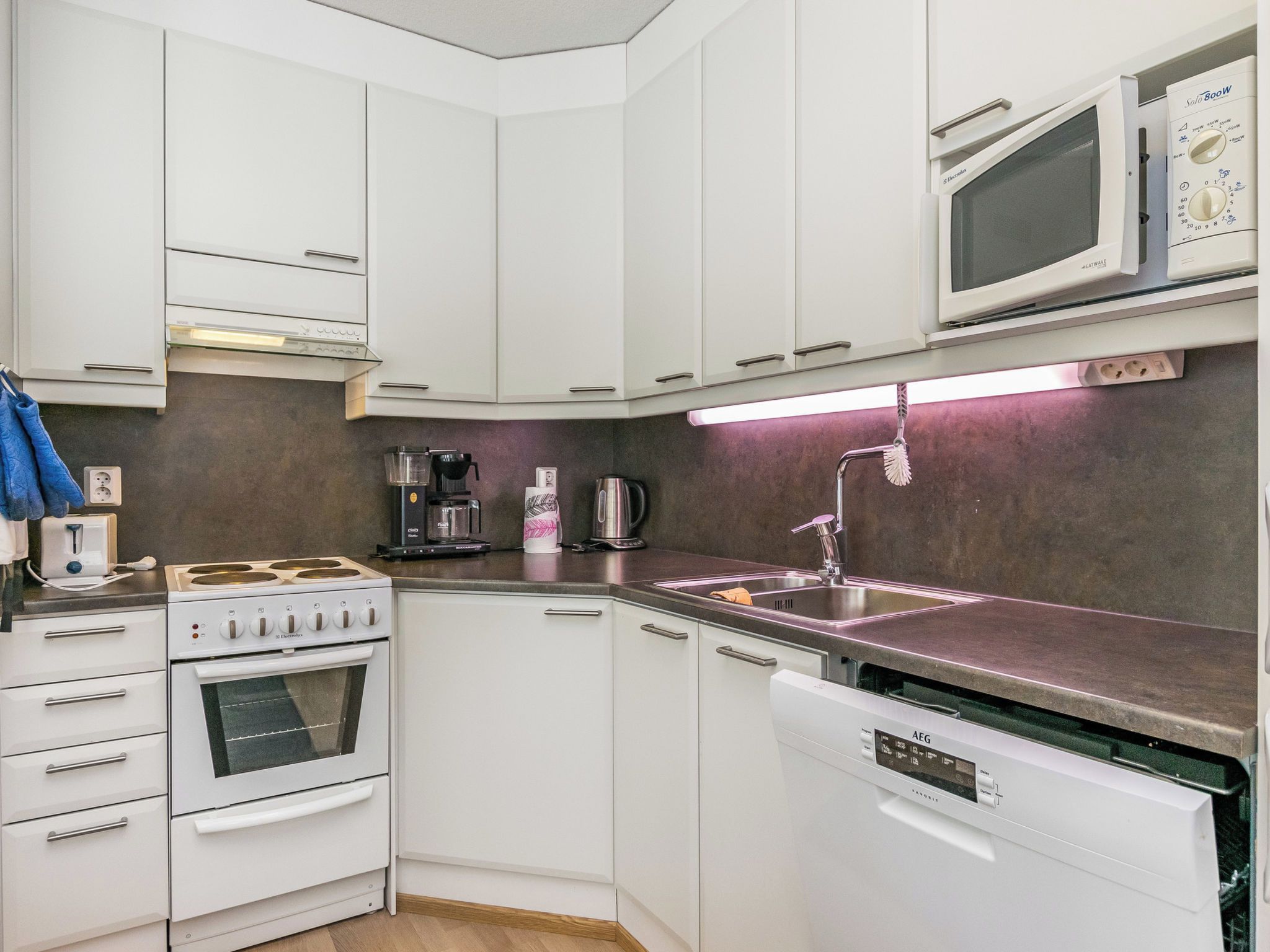A compact kitchen with white cabinets, a built-in oven, a dishwasher, a microwave, and a coffee maker.