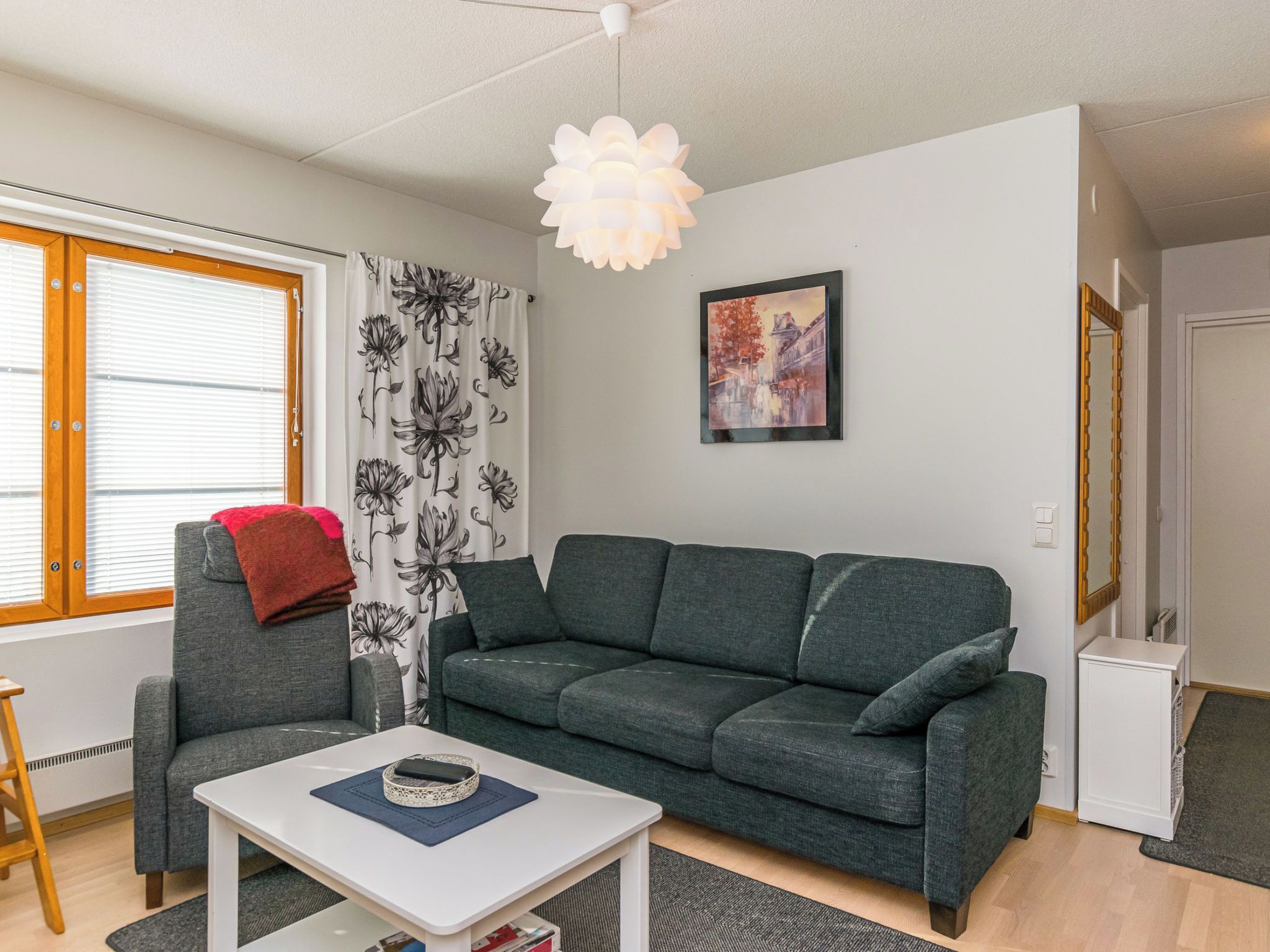 A modern living room with a grey sofa, a white coffee table, and a hanging light fixture.