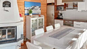Una cocina moderna con armarios blancos, un refrigerador de acero inoxidable y un microondas. Hay una zona de comedor con una mesa y sillas blancas.