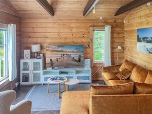 A cozy living room with a wooden interior, a large flat-screen TV, a comfortable sofa, and a small coffee table.