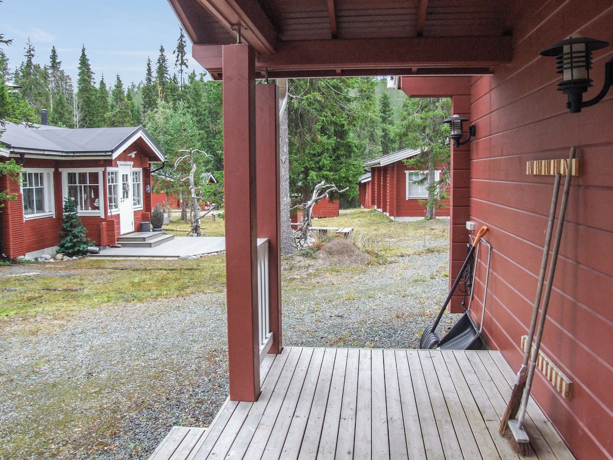 Une terrasse en bois mène à un bâtiment à l’extérieur rouge, doté d’un petit porche et offrant une vue sur une zone boisée.