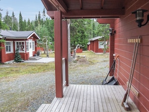 A wooden deck leading to a building with a red exterior, a small porch, and a view of a forested area. - Heikkalan helmi by Interhome (Kuusamo)