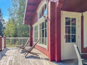 A wooden deck with two lounge chairs, a white door, and a window with a view of trees.