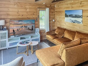 Interior acogedor de una cabaña con pared de madera, televisor, sofá y una pequeña mesa.