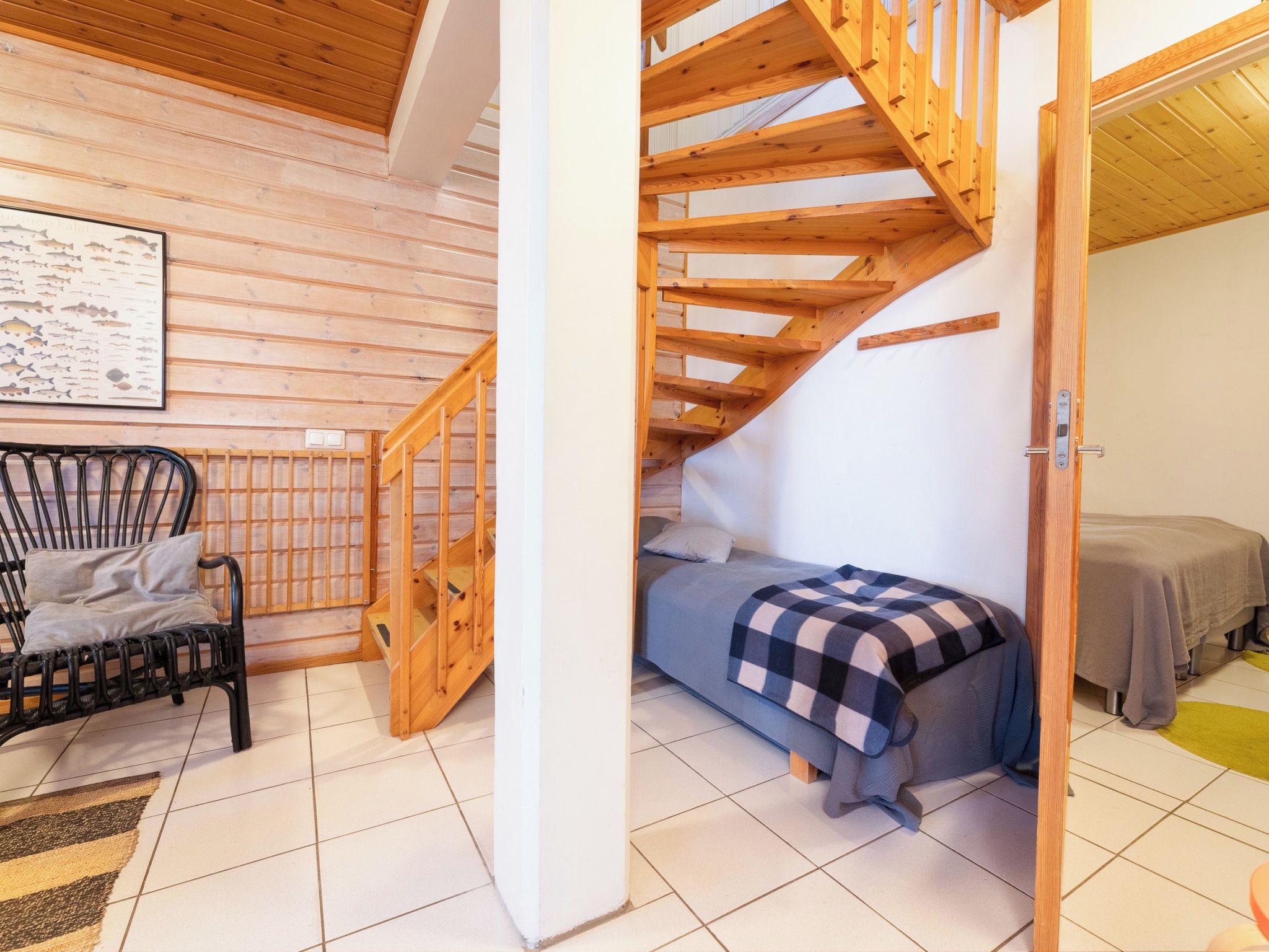 A cozy room with a wooden staircase, a bed with a checkered blanket, a chair, and a fish wall art piece.