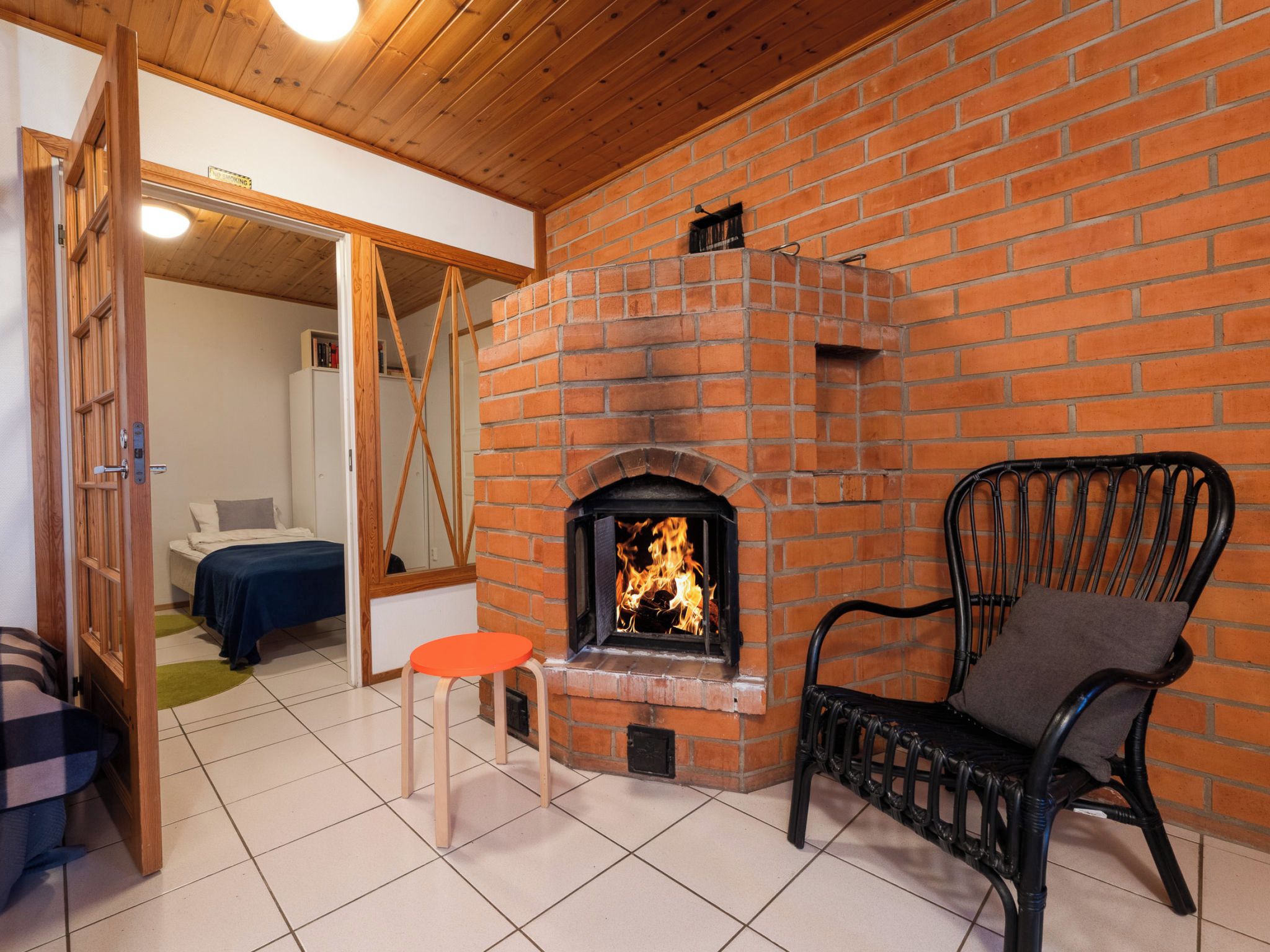 Een kamer met een schouw van baksteen, een houten plafond, een bed, een stoel en een klein tafeltje.
