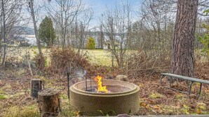 Un foyer en béton avec des flammes, entouré d’une terrasse en bois et d’un tapis violet.