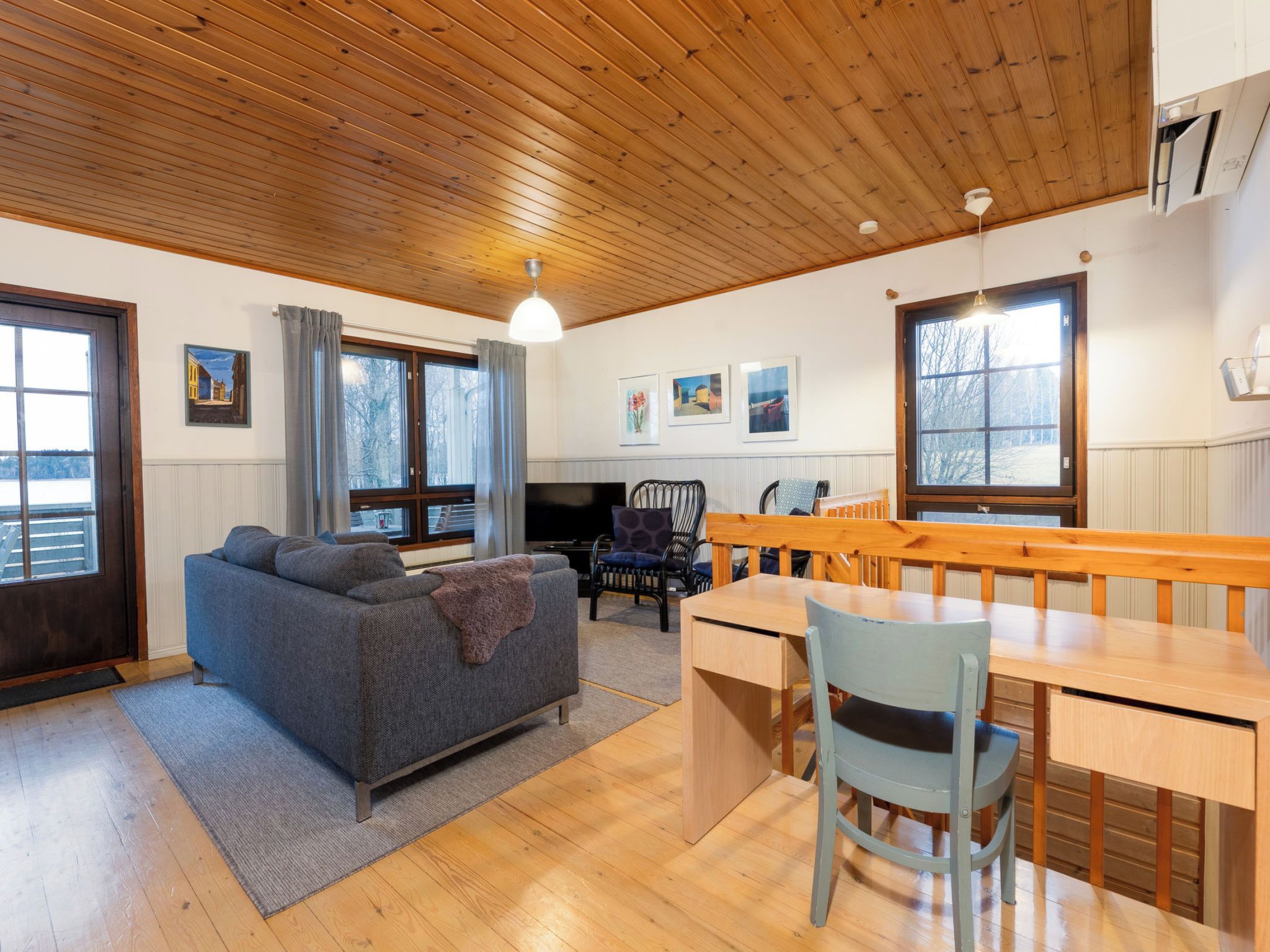 Een gezellige woonkamer met een houten plafond, een bank, een televisie en een eethoek met een tafel en stoelen.