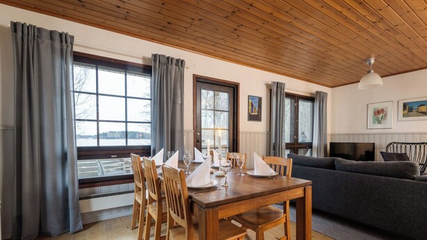 Un coin repas avec une table en bois dressée pour quatre personnes, bordé de grandes fenêtres ornées de rideaux.