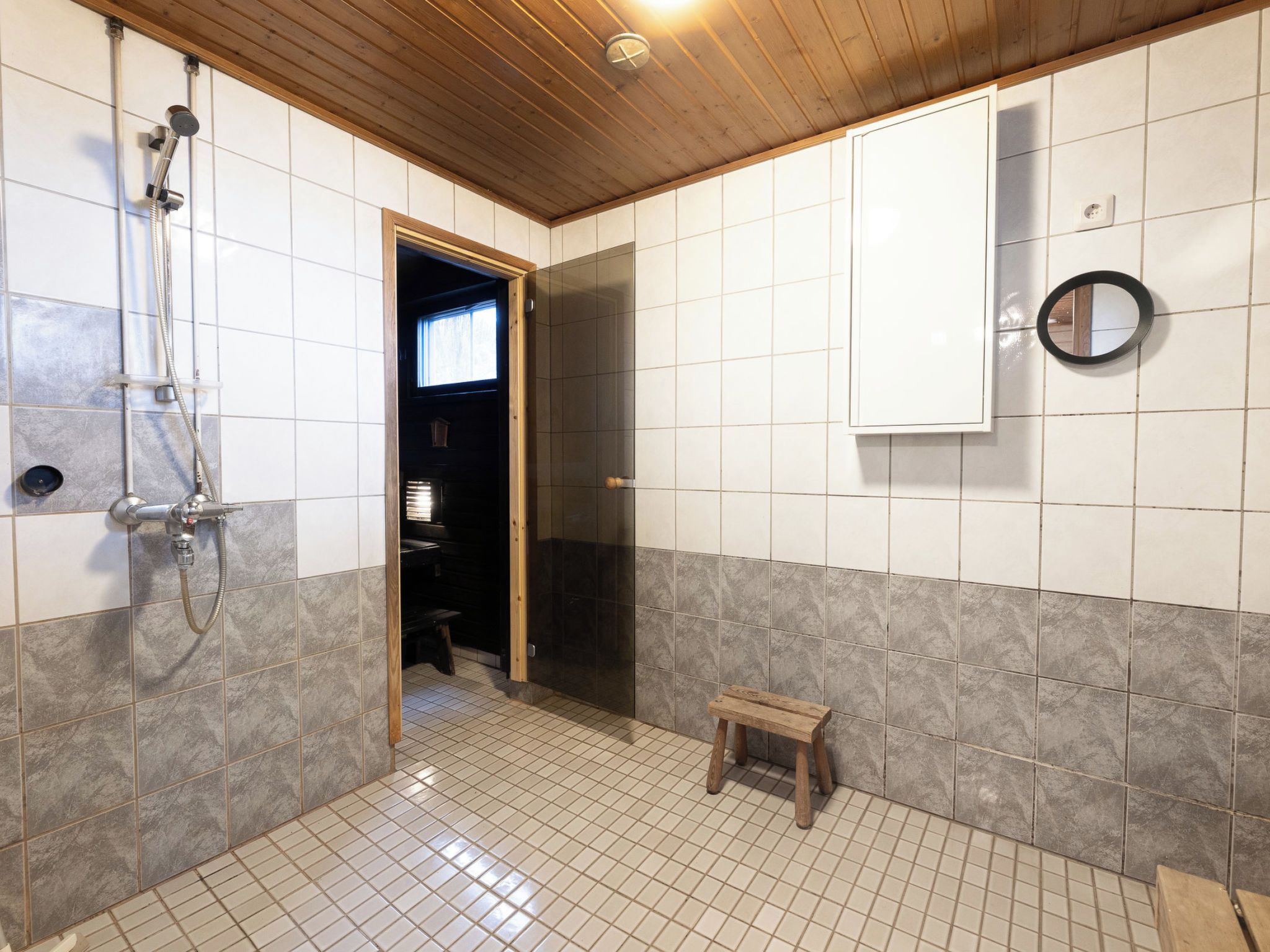 Ein Badezimmer mit einer Dusche, einem hölzernen Hocker und einem Spiegel an der Wand.