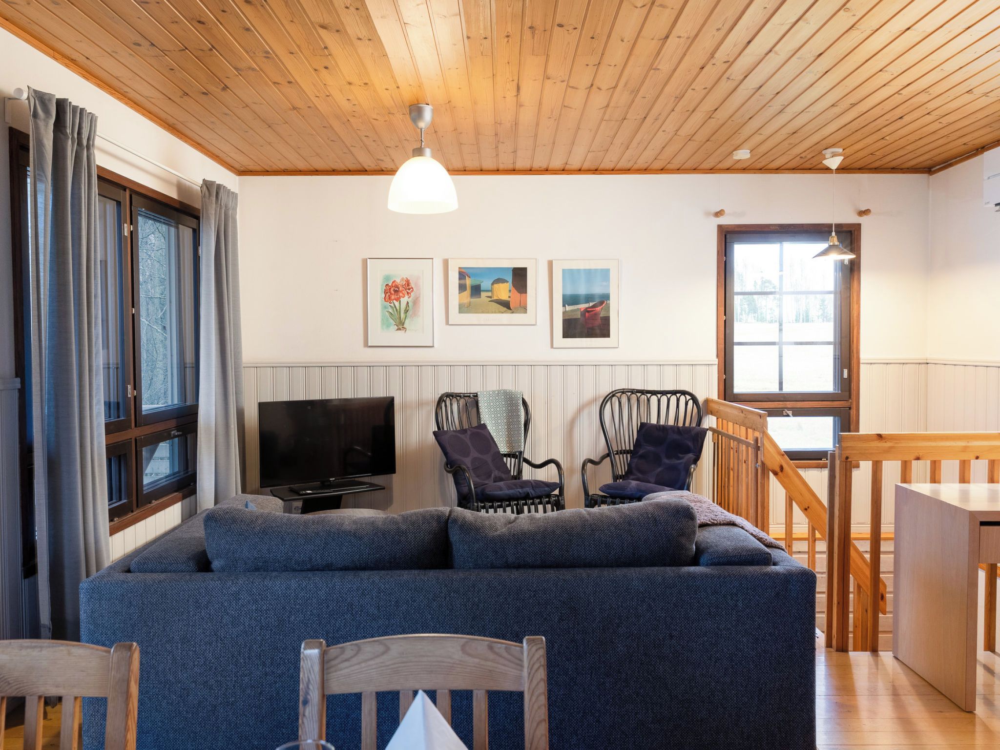 Una sala de estar acogedora con techo de madera, un televisor de pantalla plana, un sofá, dos sillones y una zona de comedor con mesa y sillas de madera.