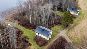 Vue aérienne d’une propriété comprenant deux maisons, entourée d’une forêt dense et bordée d’un plan d’eau.