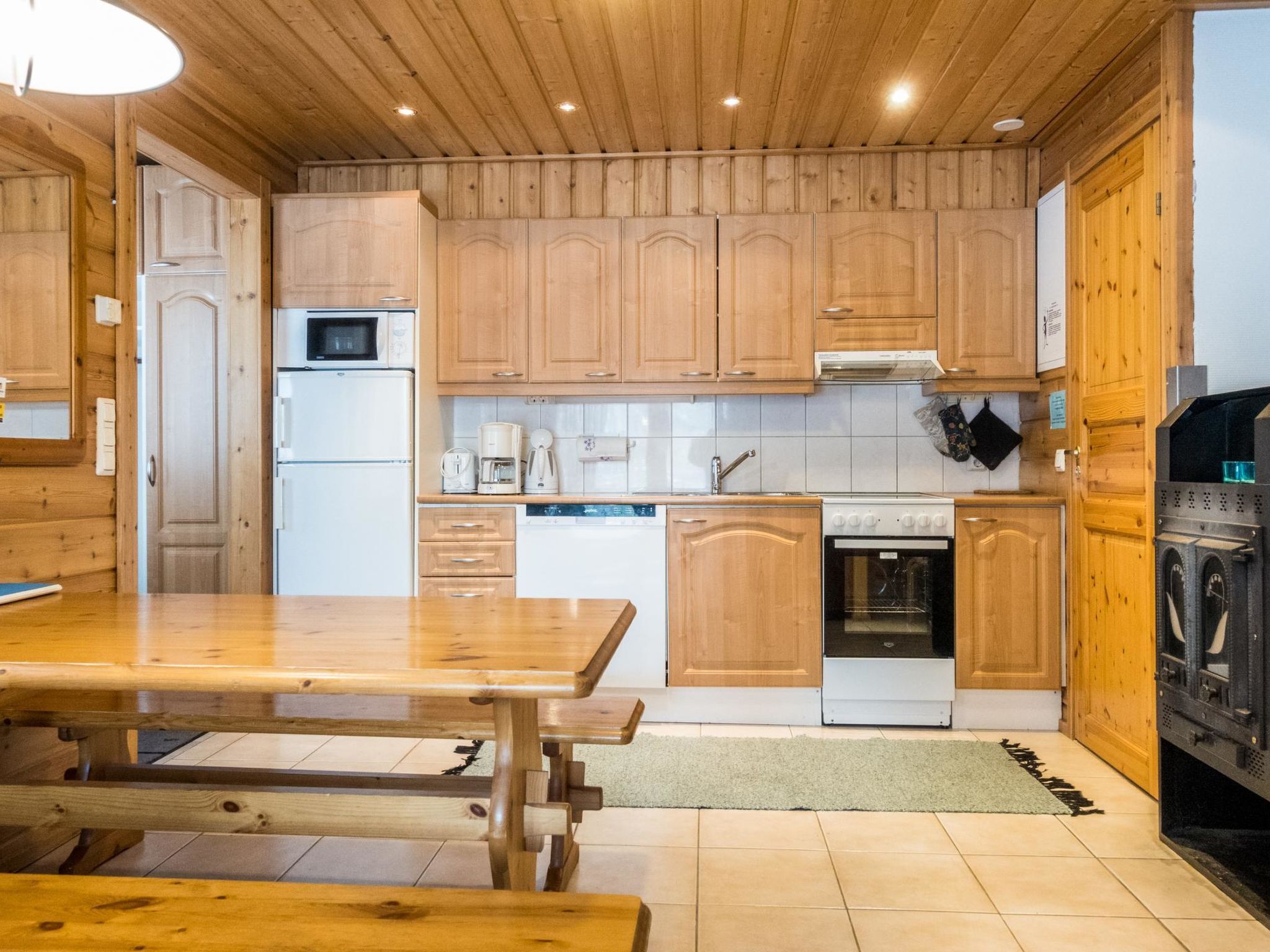 Eine Küche mit Holzschränken, einem Kühlschrank, einer Mikrowelle, einer Kaffeemaschine, einem Geschirrspüler, einem Backofen und einer Waschmaschine.