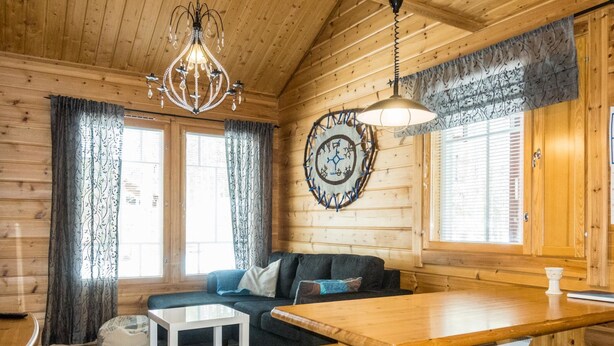 A cozy wooden cabin interior with a sofa, a wooden table, and a chandelier.