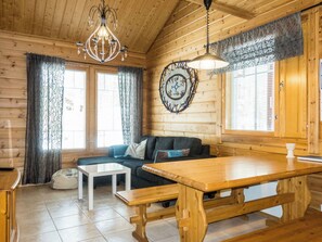 A cozy cabin interior with a wooden ceiling, a chandelier, a round wall clock, a sofa, a table, and a bench. - Hirvas levi 2 by Interhome (Kittilä)
