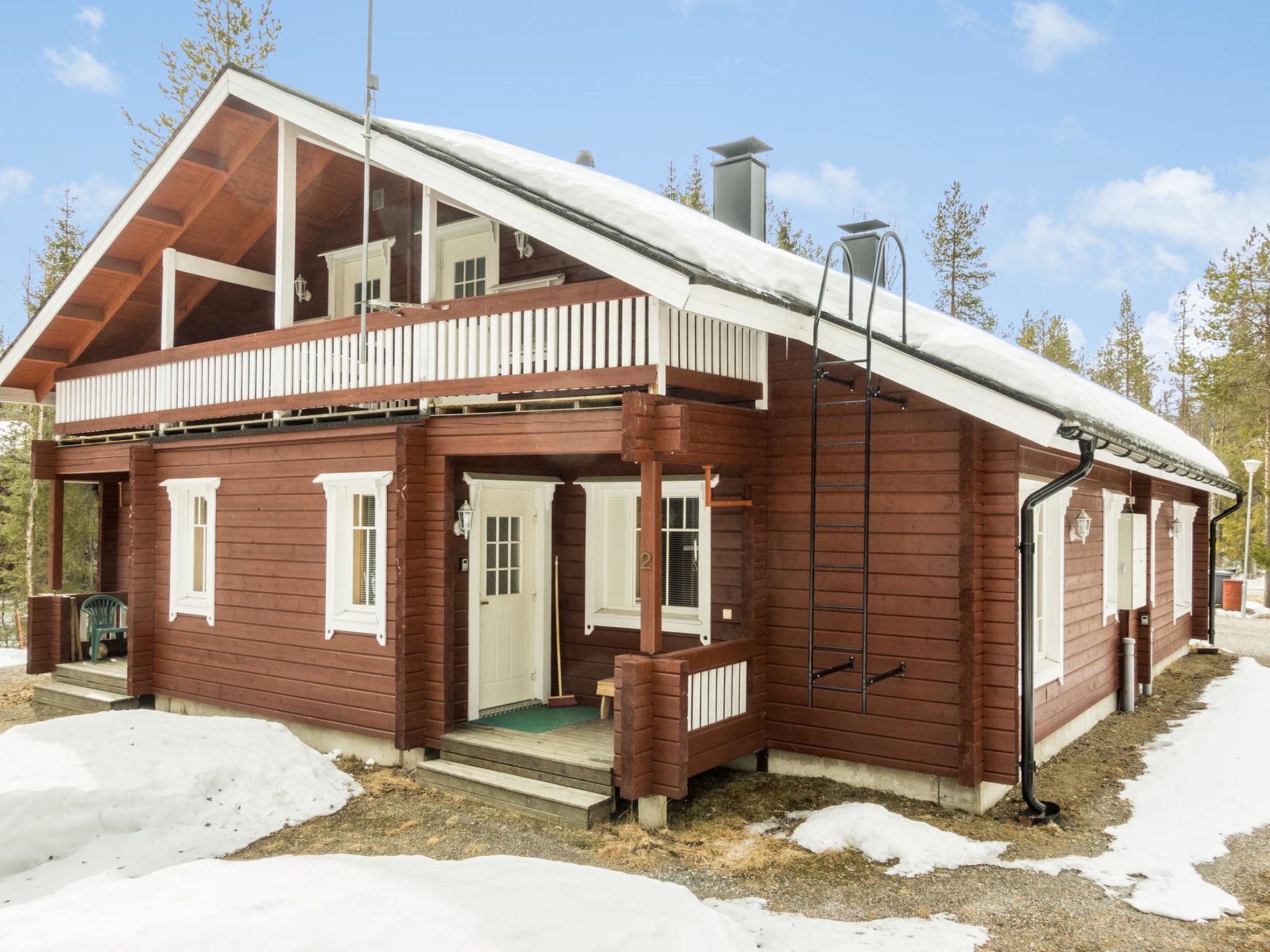 Eine zweistöckige Holzhütte mit Balkon, Schornstein und schneebedecktem Dach.