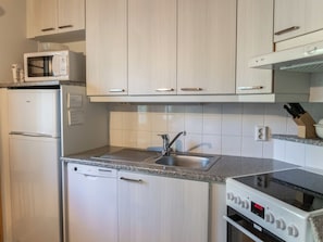Cocina compacta con armarios blancos, microondas integrado, lavavajillas, pileta y estufa.