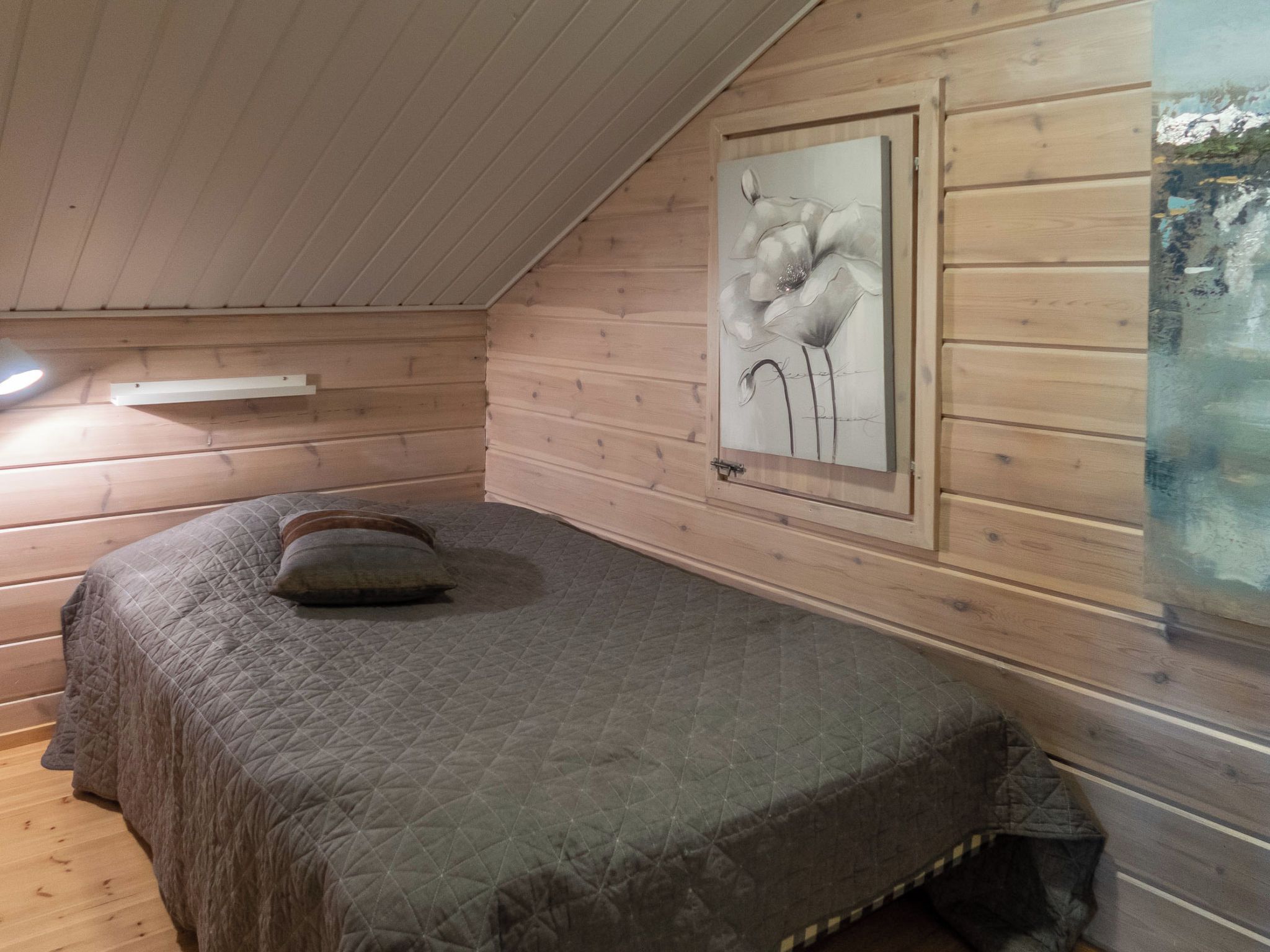 Una cama individual en una habitación tipo cabaña de madera con una obra enmarcadas en la pared.