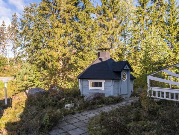 A small cabin with a dark roof, surrounded by dense forest.