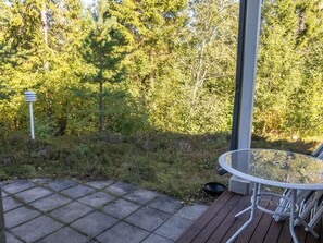 An outdoor patio with a glass table and chairs, surrounded by a wooden deck and a stone pathway. - Jeskatti by Interhome (Sotkamo)