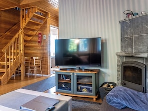 A living room with a television, fireplace, wooden staircase, and a cozy seating area. - Jeskatti by Interhome (Sotkamo)