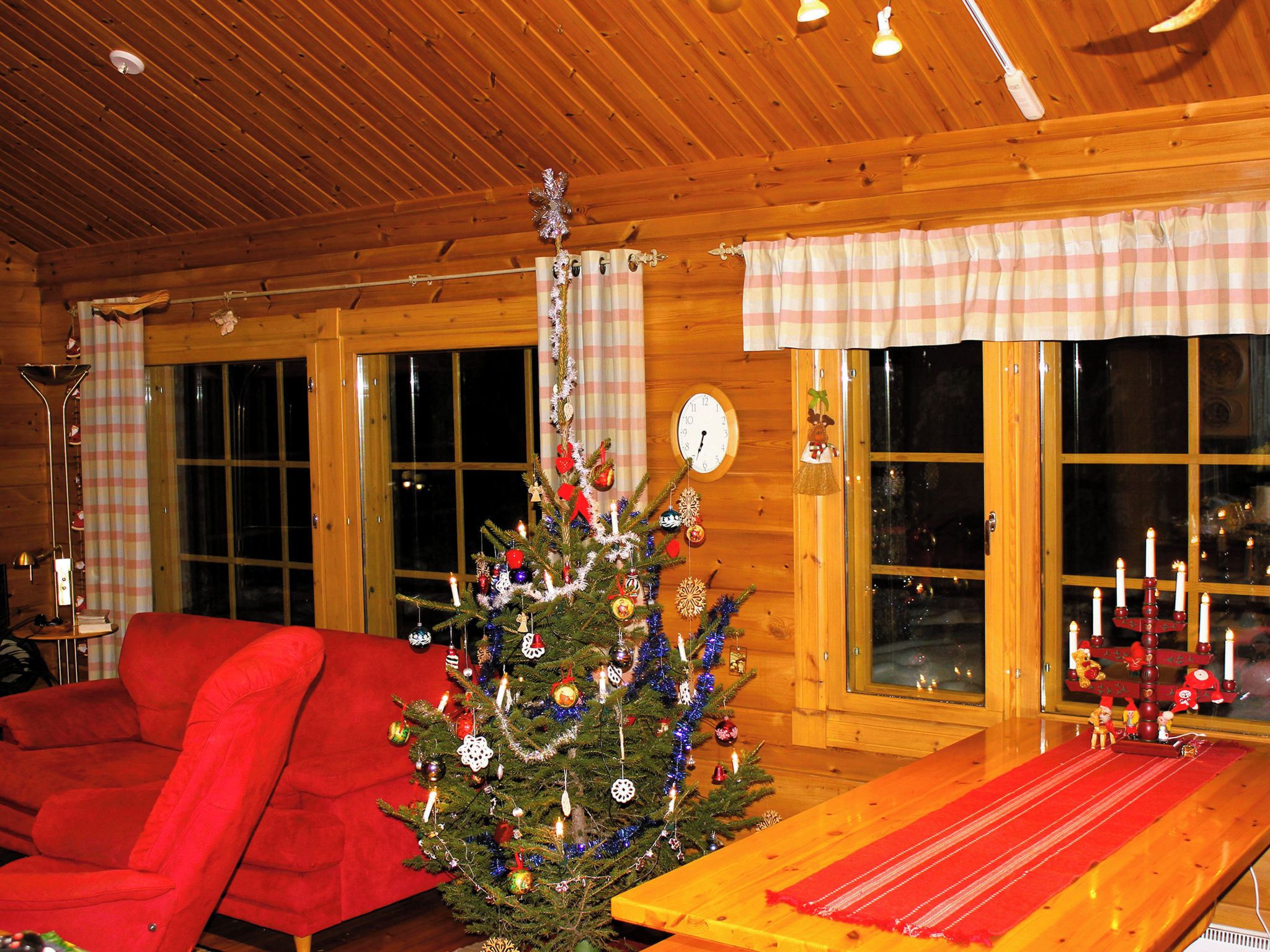 Ein gemütliches Zimmer mit Holzbalkendecke, einem roten Sofa, einem Weihnachtsbaum und einem Tisch mit roter Tischläufer.