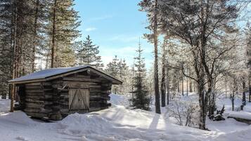 Lumihuntuun peittynyt metsä ympäröi hirsihökkelöä.