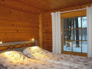 Une pièce de cabane en bois comprenant un lit, une fenêtre avec des rideaux et une vue sur un paysage enneigé.