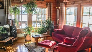 A cozy cabin interior with wooden walls, a red sofa, multiple potted plants, and a television. - Hamppulahti by Interhome (Kuhmo)