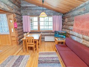 Een interieur van een blokhut met een eettafel, stoelen, een bank, een televisie en een raam met gordijnen.