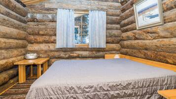 A log cabin bedroom with a bed, a small table, and a window with curtains.