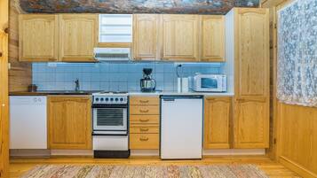 A compact kitchen with wooden cabinets, a stove, a microwave, and a coffee maker.