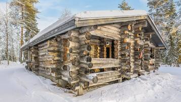 A log cabin with a snow-covered roof, surrounded by snow and trees.